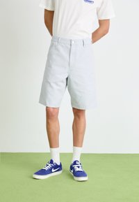 Lichtblauwe katoenen shorts met een relaxed fit, voorzien van een knoopsluiting aan de voorkant en zijzakken, gecombineerd met witte sokken en blauwe sneakers.