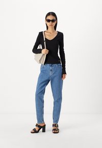 Μαύρο μακρυμάνικο τοπ με V-λαιμόκοψη, ανοιχτό μπλε τζιν, μαύρες ψηλές σандalias και μπεζ τσάντα ώμου. Τα αξεσουάρ περιλαμβάνουν σκούρα γυαλιά ηλίου.