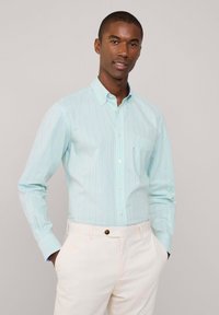 Lichtblauw en wit gestreepte blouse met lange mouwen, een button-down kraag en een borstzak, gecombineerd met crèmekleurige broeken.