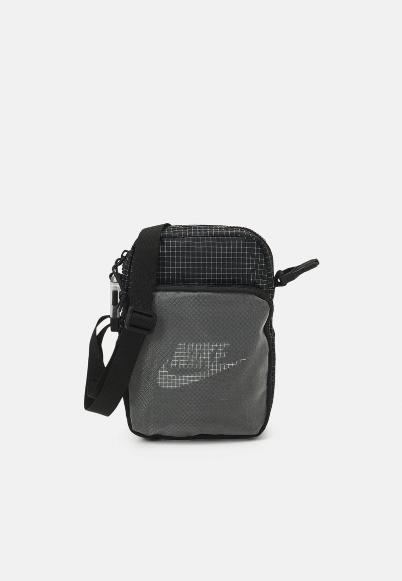Black and grey Nike shoulder bag, featuring a grid pattern top, reflective logo, adjustable strap, and zip closure. Compact design.