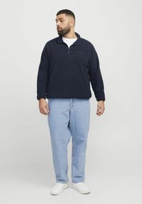 Marineblå fleece quarter-zip pullover, tekstureret stof, broderet logo, parret med lyseblå lige ben jeans og hvide sneakers.