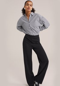 Ohlapne črne hlače v kompletu s črtastim srajčnim zgornjim delom v črni in beli barvi. Imajo ukrivljen rob in manšete.