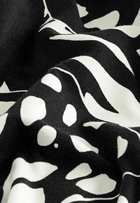 Tissu noir avec des motifs floraux et feuilles abstraits blancs, présenté en gros plan avec une texture et des plis visibles.