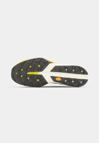 Semelle d'une chaussure de sport jaune et noire avec une bande de roulement texturée et un logo Vibram orange sur fond blanc.
