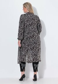 Leopardmönstrad lång kavaj med långa genomskinliga ärmar, bärs över svarta leggings med strassprydnader och utskärningar. Svarta klackar synliga.