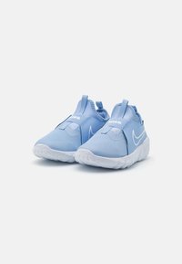 Un paio di sneakers slip-on Nike di un blu chiaro con suole bianche e linguette di presa, posizionate su uno sfondo bianco semplice.