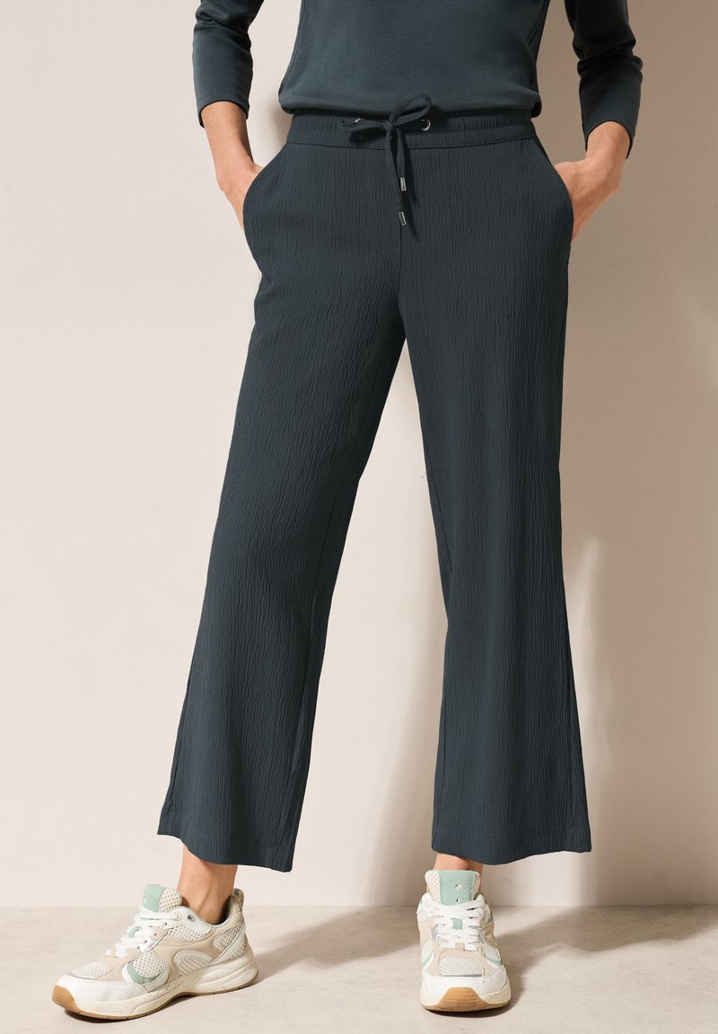 Pantalons larges texturés gris foncé avec une taille élastique et un cordon de serrage. Associés à des baskets blanches et menthe, affichant un look décontracté.