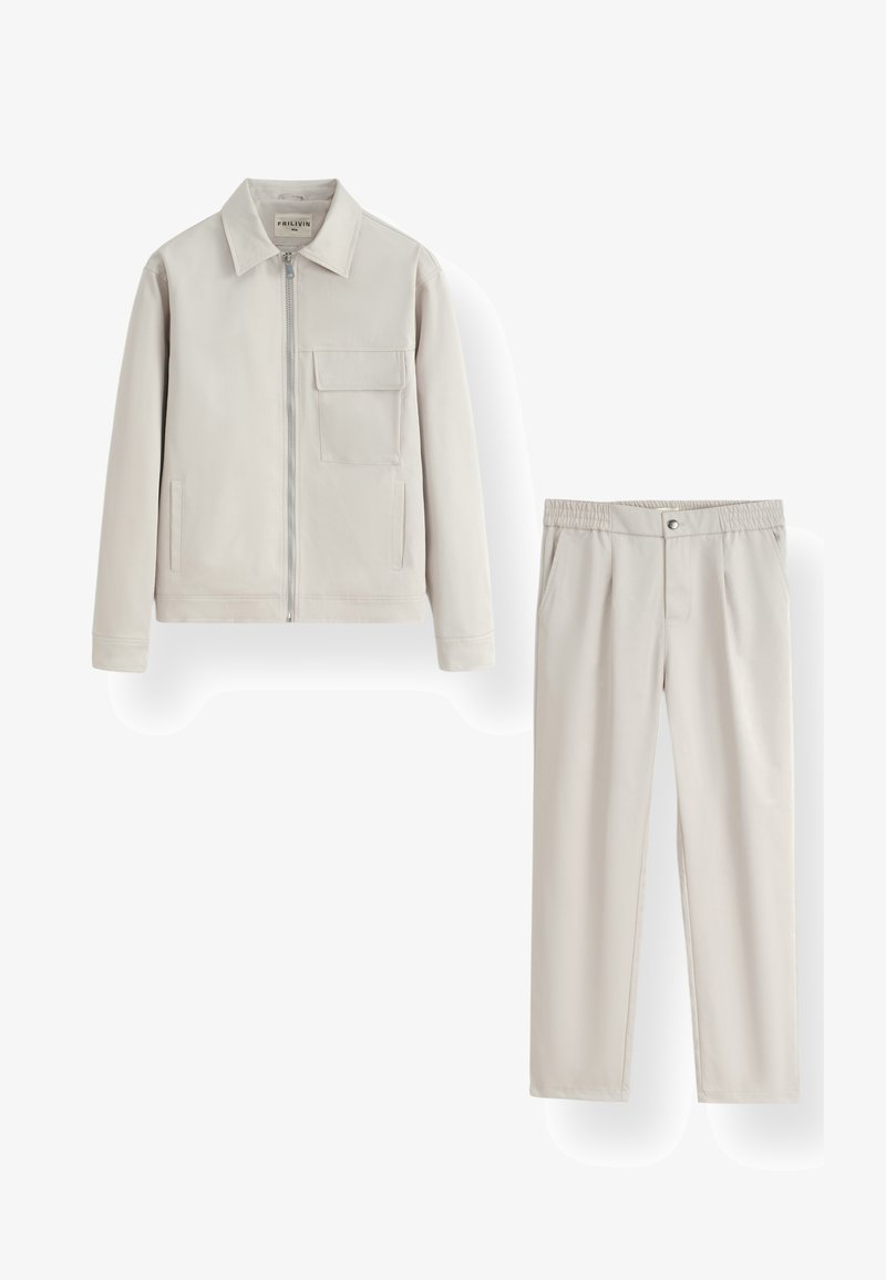 Veste zippée beige clair avec col et poche poitrine, assortie à un pantalon élastique à taille.