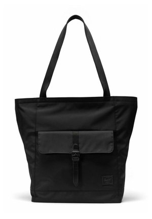 Sac fourre-tout noir avec de longues anses, poche à rabat à l'avant sécurisée par une boucle, et une petite étiquette logo rectangulaire dans le coin inférieur.