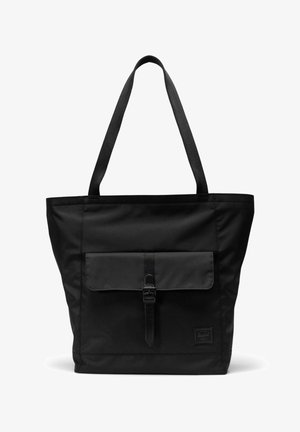 Sac fourre-tout noir avec de longues anses, poche à rabat à l'avant sécurisée par une boucle, et une petite étiquette logo rectangulaire dans le coin inférieur.