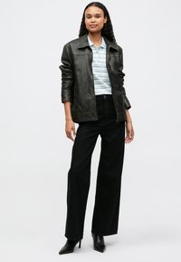 Μαύρο δερμάτινο μπουφάν πάνω από ανοιχτό μπλε παντελόνι πόλο με ρίγες, σε συνδυασμό με ψηλόμεσα μαύρα παντελόνια με φαρδιές ίνες και μαύρες μυτερές γόβες.