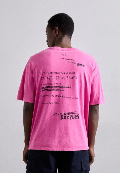 Pink cotton t-shirt with oversized fit. Features abstract text and graphics in black on the back. Short sleeves and round neck design.