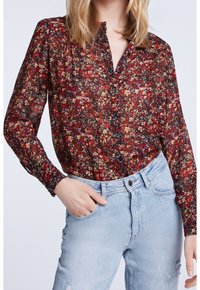 Blouse noire transparente avec un motif floral coloré, devant à boutons, manches longues et poignets froncés, associée à un jean taille haute bleu clair.