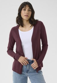 Burgunderfarget cardigan med åpen front, lange ermer og ribbede mansjetter, sammen med en hvit tank top og høy midje blå jeans.