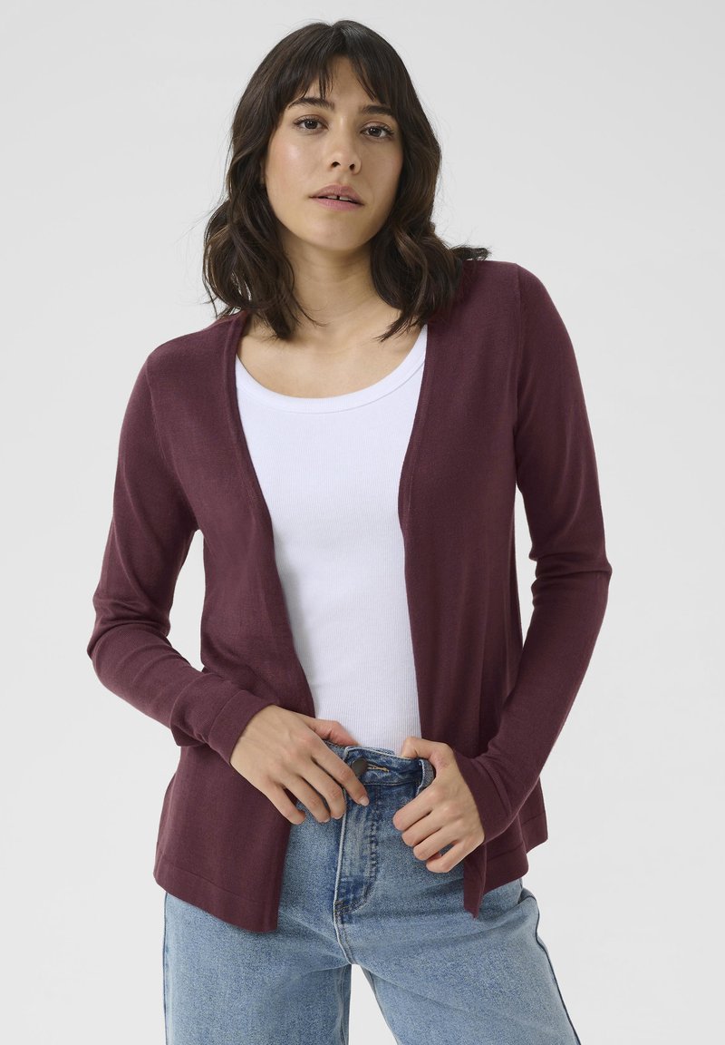 Burgunderfarget cardigan med åpen front, lange ermer og ribbede mansjetter, sammen med en hvit tank top og høy midje blå jeans.
