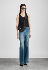 Melna bezpiedurkņu topiņš, augstas jostas līnijas platās bikses, melna rokassoma ar zelta akcentiem un stūraini melni saulesbrilles. Gludas tekstūras.