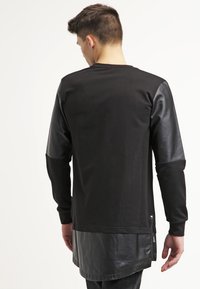 Top lungo nero a maniche lunghe con corpo in cotone e maniche in pelle, orlo curvo e dettaglio con zip laterale. Adatto per abbigliamento casual.