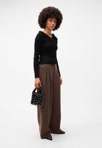Sort ribbet zip-up sweater, brede brune bukser og en sort taske med nitter. Spidse sorte sko fuldender outfittet.