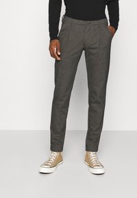 Grijze textuurbroek met een getailleerde pasvorm, voorzien van steekzakken aan de voorkant en een knoopsluiting, gecombineerd met lichtbeige hoge sneakers.