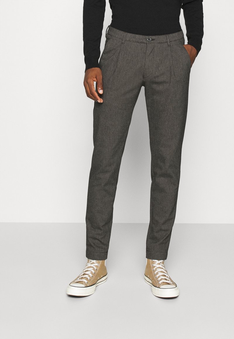 Grijze textuurbroek met een getailleerde pasvorm, voorzien van steekzakken aan de voorkant en een knoopsluiting, gecombineerd met lichtbeige hoge sneakers.