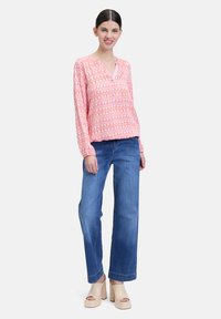 Blouse rose à manches longues avec un motif géométrique, associée à un jean bleu à jambes larges et des talons compensés beiges. Coupe décontractée avec un décolleté en v.