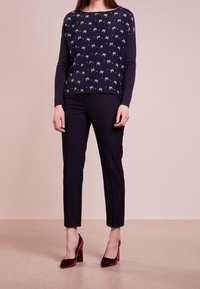 Maglione blu navy a maniche lunghe con motivo a fiocchi bianchi, abbinato a pantaloni neri e scarpe con tacco bordeaux. Tessuto morbido, vestibilità comoda.