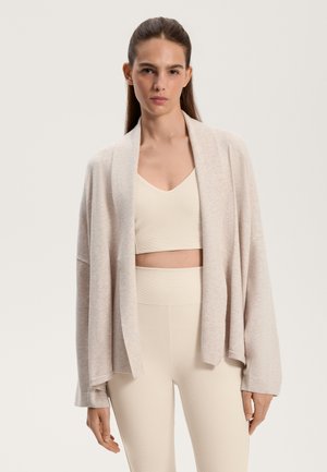 Light beige open-front cardigan, soft knit texture, relaxed fit, dropped shoulders, worn over a matching crop top and leggings.