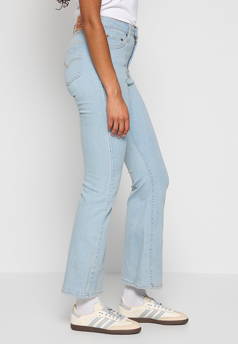 Hellblaue Schlagjeans mit hoher Taille, dezentem Verblassen und klassischem fünf-Taschen-Design. Kombiniert mit cremefarbenen und grauen Turnschuhen.