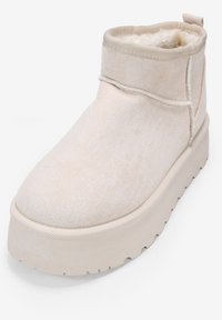 Botín beige hasta el tobillo hecho de suave ante con un alto cuello, forro de felpa y suela de plataforma gruesa con lados texturizados.