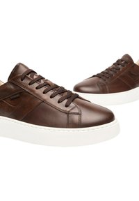 Le sneakers in pelle marrone presentano una texture liscia, suola in gomma bianca, punta rotonda e lacci piatti. Il pannello laterale include dettagli perforati.