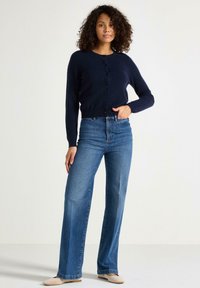 Cardigan bottoni navy realizzato in tessuto morbido, abbinato a jeans a gamba larga blu chiaro. Design semplice, texture uniforme e senza motivi visibili.