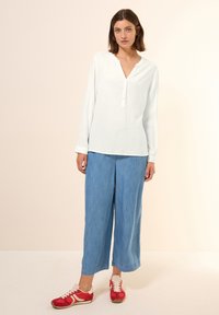 Witte blouse met lange mouwen en V-hals, gecombineerd met lichtblauwe wijde broek en rode sneakers met witte accenten. Zachte, lichtgewicht texturen.