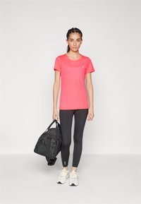 Lett rosa trenings T-skjorte, svarte leggins og hvite sportssko. Svart duffelbag med tekstilstruktur; enkel design, ingen synlige logoer.