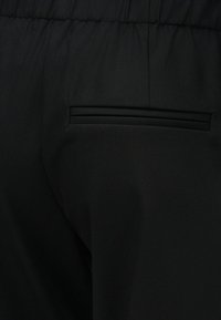 Μαύρο παντελόνι από ύφασμα με ελαστική μέση και οριζόντια τσέπη welt στο πίσω δεξί μέρος.