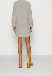 Abito maglione in grigio chiaro con silhouette strutturata, orlo a coste e maniche a palloncino. Indossato con stivali alla caviglia gialli.