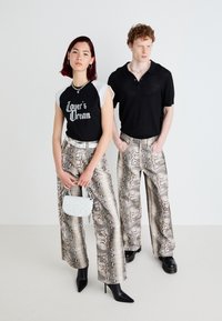 T-shirt grafico in bianco e nero, pantaloni a gamba larga con stampa di serpente e décolleté nere appuntite. Presente una piccola borsa grigia chiara e accessori in argento.