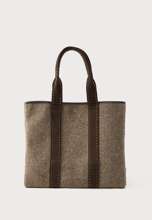 Sac de mână din țesătură maro și bej, cu două mânere lungi maro și cusături albe vizibile pe un fundal alb.