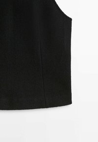 Vêtement noir sans manches en tissu texturé avec un ourlet droit, présenté sur un fond blanc.