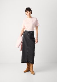 T-shirt di cotone rosa chiaro con maniche corte e logo, abbinato a una gonna maxi in denim nera a vita alta e stivali in stile western color cammello.
