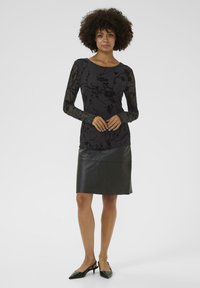 Sort langærmet top med blomsterdesign, parret med en sort læderpencilskirt. Outfittet har en tætsiddende design og glat struktur.
