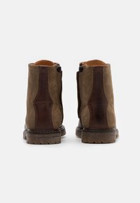 Bottines marron en mélange de daim et de cuir, avec des fermetures éclair sur le côté, des textures contrastées et une semelle robuste pour l'adhérence.
