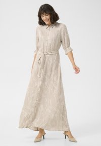 Robe longue beige avec un motif en vagues, col classique, ouverture à boutons et taille ajustable à nouer. Tissu léger avec des manches retroussées.
