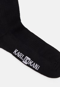 Fekete pamutzokni bordázott mintával és fehér "KARL KANI" logóval a szélén. Egyszerű dizájn klasszikus fazonnal.