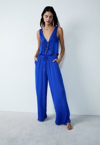 Ensemble deux pièces bleu comprenant un haut à col en V avec un détail noué et un pantalon large avec une taille élastique et des poches latérales.