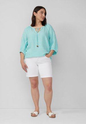 Turquoise gestreepte blouse met een striknek, gecombineerd met witte gerolde shorts en witte sandalen met een metalen accent.