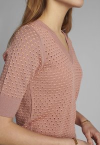 V-ringad, kortärmad tröja i mjuk rosa med texturerade, upphöjda prickar överallt. Tillverkad av lätta material med ribbade detaljer.