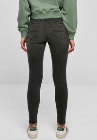 Jeans negros ajustados con tiro alto, que presentan bolsillos traseros y un deslavado sutil. Combinados con zapatillas color crema con detalles en verde.