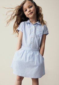 Robe en vichy bleu avec des manches courtes, un devant �à boutons et une taille élastique. Elle comprend des poches latérales et une petite poche sur la poitrine.