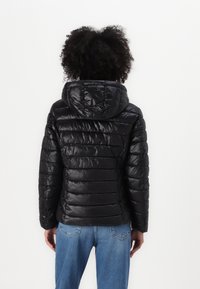 Zwarte pufferjack met een capuchon, met geborduurde lijnen en een glanzende afwerking, gecombineerd met casual blauwe spijkerbroeken.