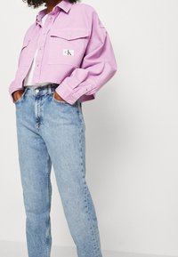 Ljuslila kort denimjacka med två bröstfickor och en varumärkesetikett, kombinerad med högmidjade ljusblå jeans.